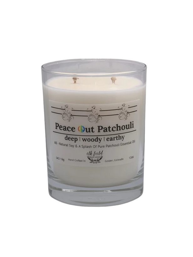 A glass jar candle with white wax and a clear lid, featuring a label that reads 'Peace Out Patchouli' and 'deep woody earthy'.