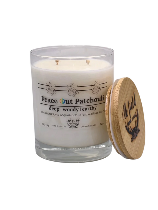 A glass jar candle with off-white wax and two wicks, labeled 'Peace Out Patchouli', shown next to a round natural bamboo lid on a plain white background.